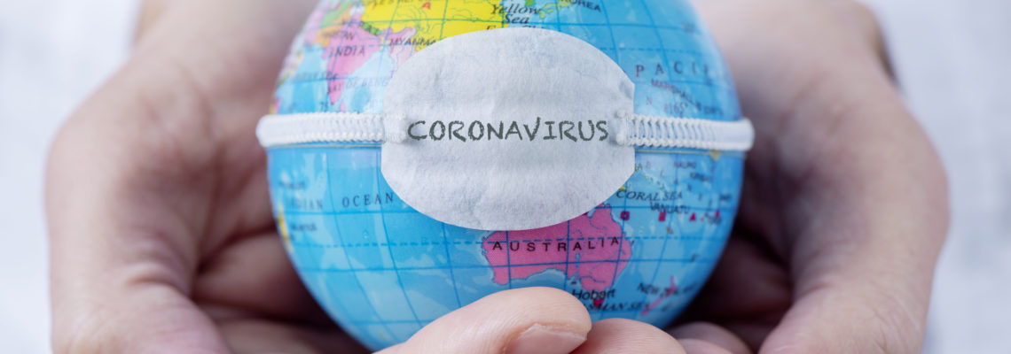 Closeup of a caucasian doctor man holding a world globe with a protective mask with the word coronavirus written in it