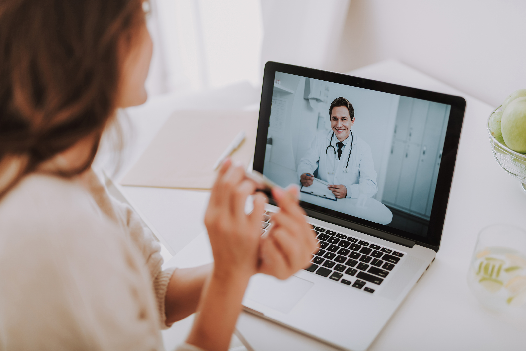 Cropped back rear view of expectant mother sitting in light living room and using pc laptop while talking with smart doctor. She showing pregnancy test in camera