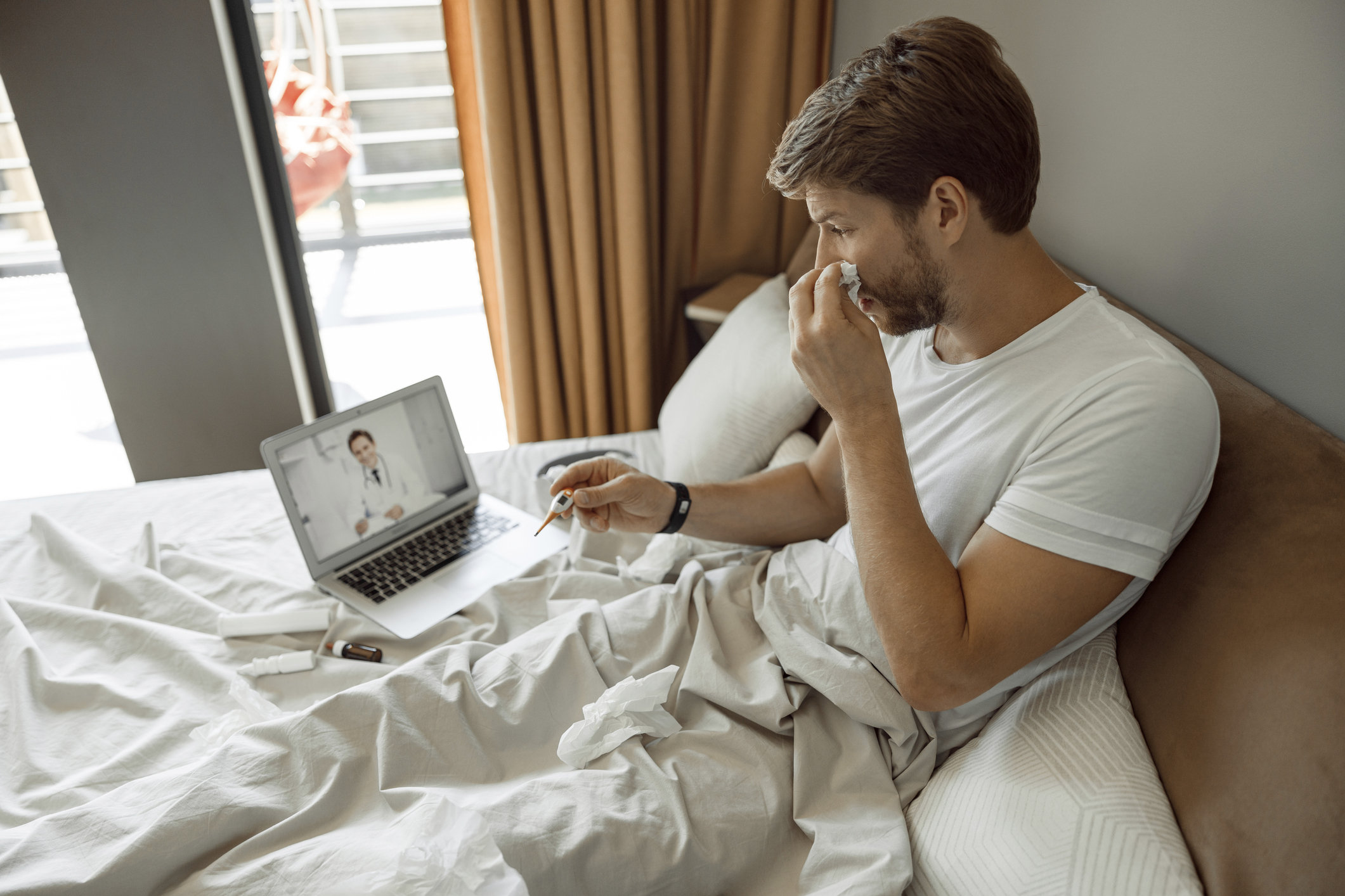 Sick young male blowing his nose talking to a doctor